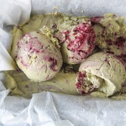 Scoops of matcha blackberry semifreddo sits in a tin lined with paper on a dark background.