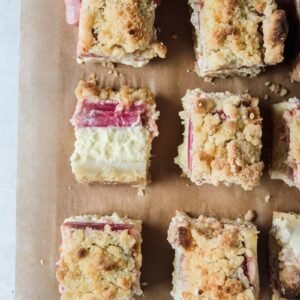 Estonian rabarbi kohupiimakook - Rhubarb Streusel Cheesecake square slices sit on brown baking paper with one piece laying on it's side for a view of the cheesecake and bright rhubarb hidden beneath the streusel topping.