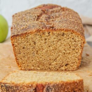 The light crumb of a Apple butter Cake is visible while sitting on parchment paper with a brown cloth behind.