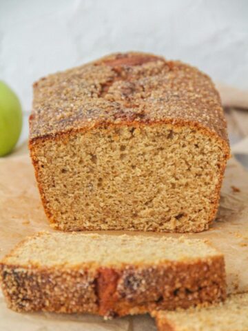 The light crumb of a Apple butter Cake is visible while sitting on parchment paper with a brown cloth behind.