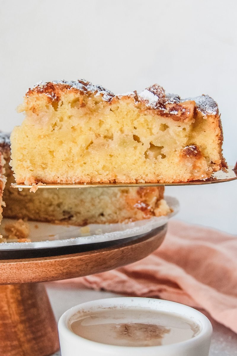 A slice of Irish apple cake sits on a cake server with a cubes of apple visible in the center.