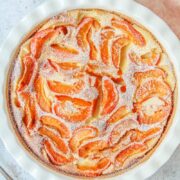 Apricot Clafoutis sits in a round white ceramic baking dish on a light gray surface.
