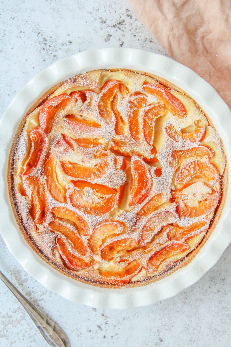 Apricot Clafoutis sits in a round white ceramic baking dish on a light gray surface.