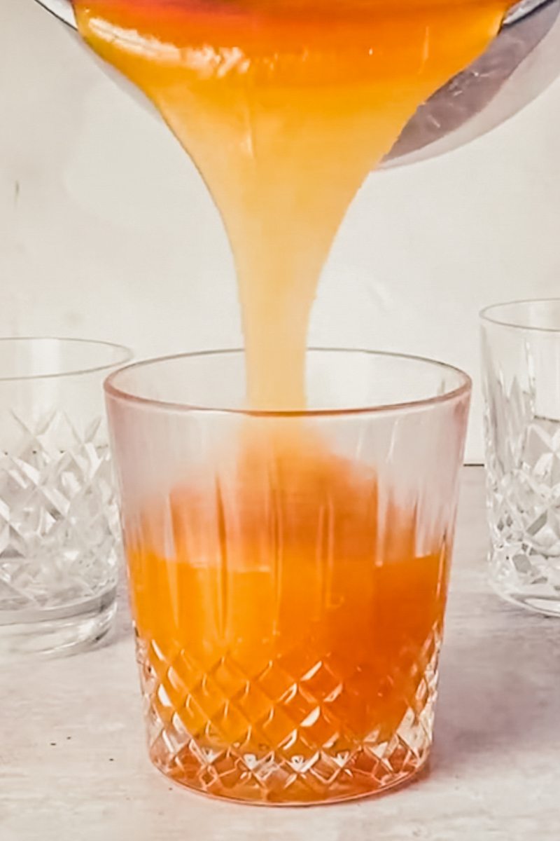 Orange pudding is poured into a serving glass on a gray surface.