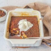 Banana Butterscotch pudding sits in a rectangle baking dish topped with scoops of vanilla ice cream on a light gray surface with a brown cloth behind.