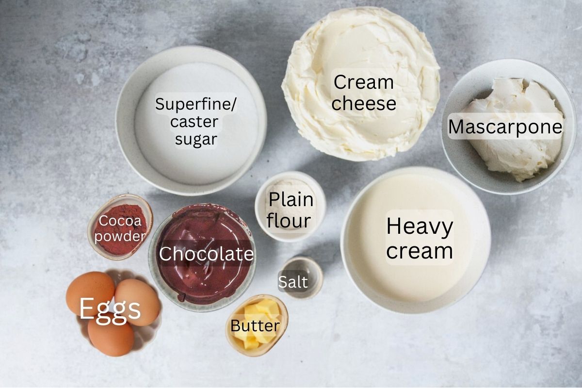 Ingredients for Basque Chocolate Cheesecake sit in a series of bowls and plates on a gray surface.