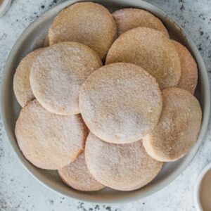 Biscochito cookies sit stacked on a rimmed ceramic gray plate on a gray surface.