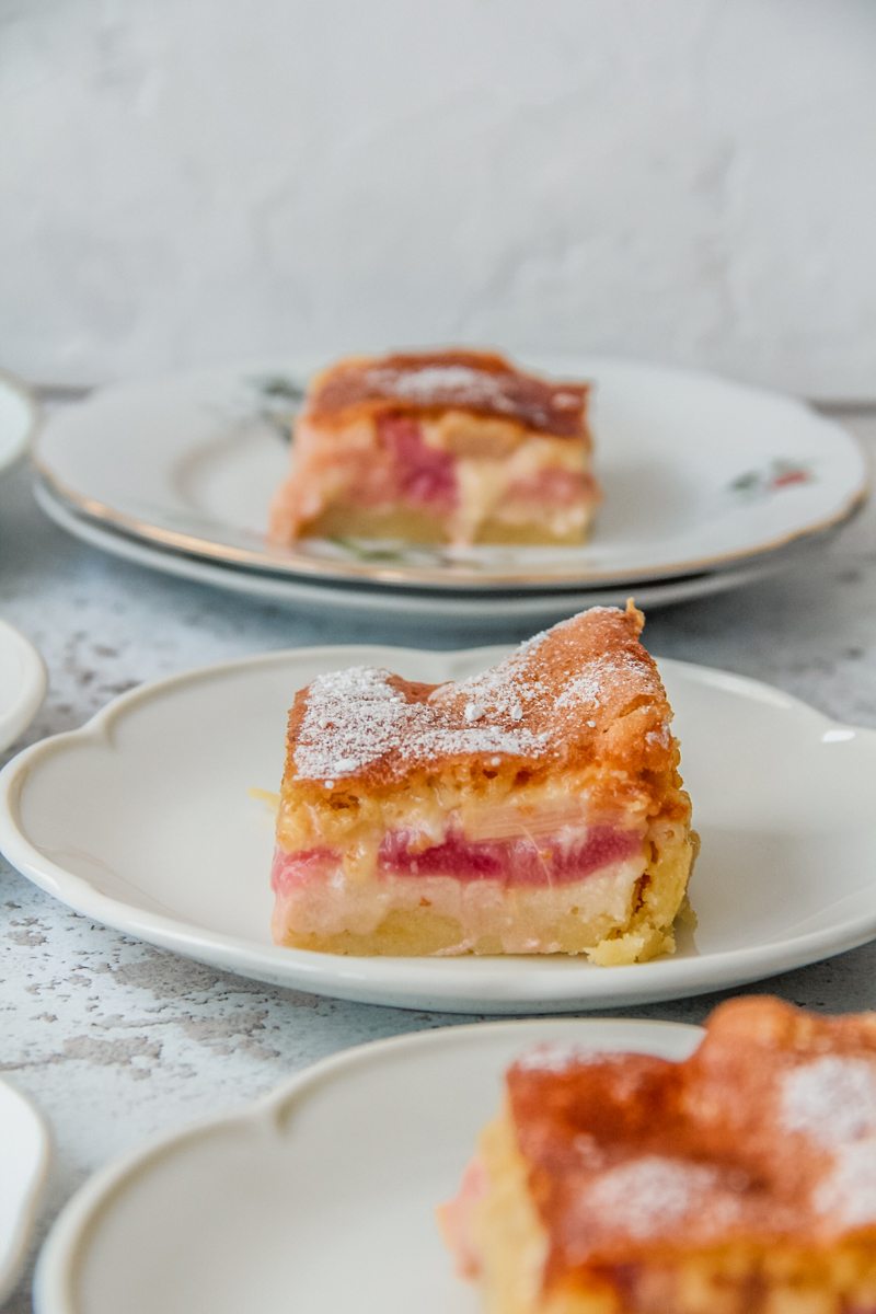The three layers of Estonian rhubarb cake sit on a fluted white ceramic plate on a light gray surface.