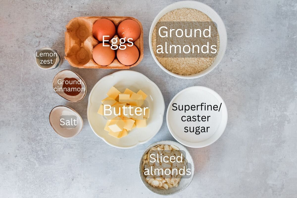 Ingredients for Portuguese almond cake sit in a variety of bowls and plates on a gray surface.