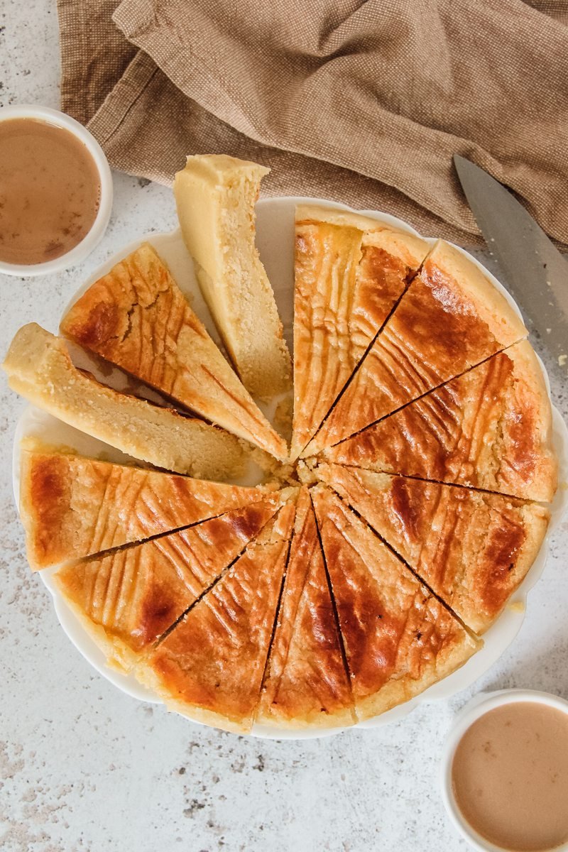 Boterkoek or Dutch Butter Cake cake sits sliced up on a white plate above a gray surface.