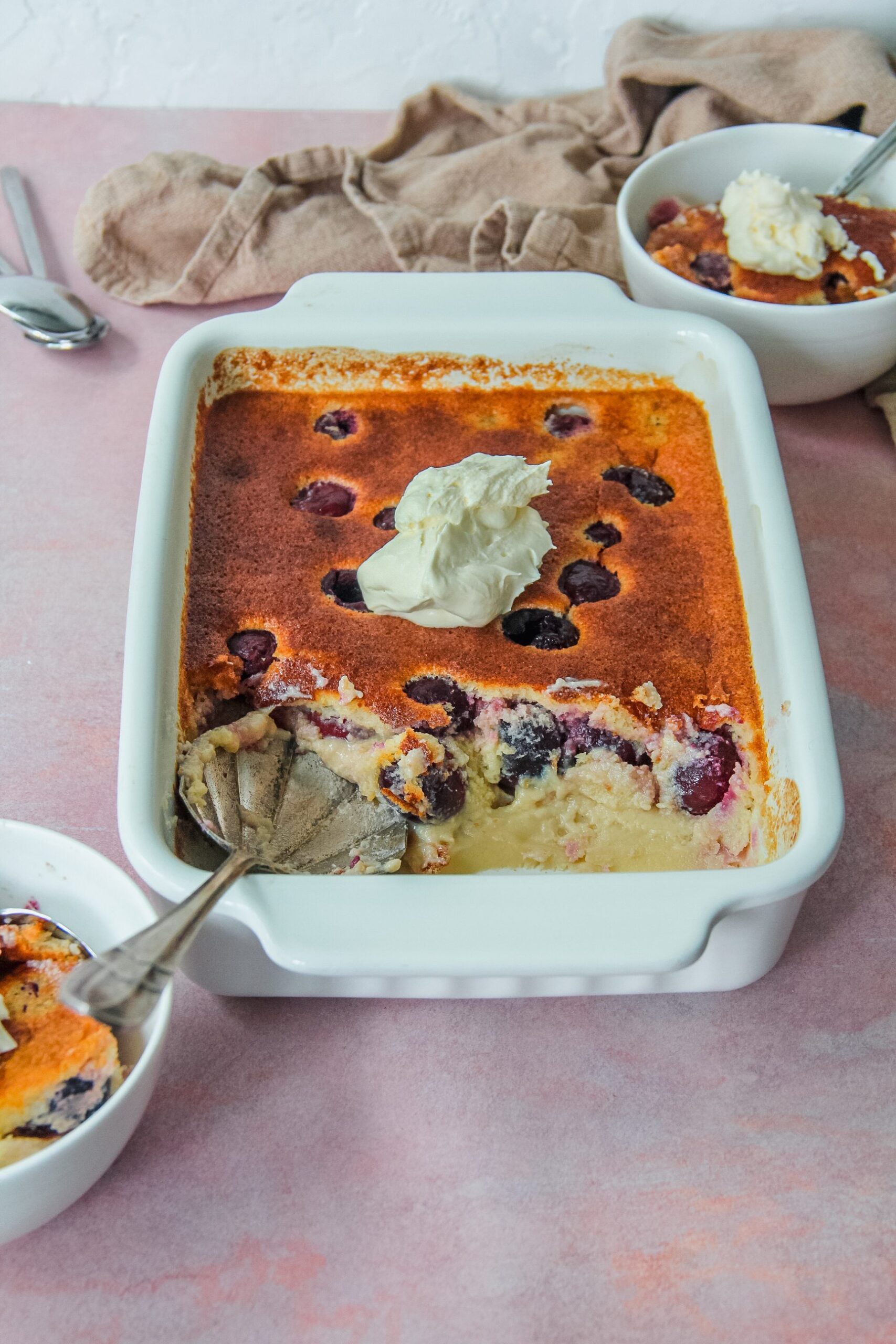 A side view of British Kentish Cherry Batter Pudding with a few individual servings on the sides on a light pink surface.