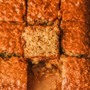 A slice of Ginger Parkin sits leaning against the remaining cake slices on a parchment lined surface.