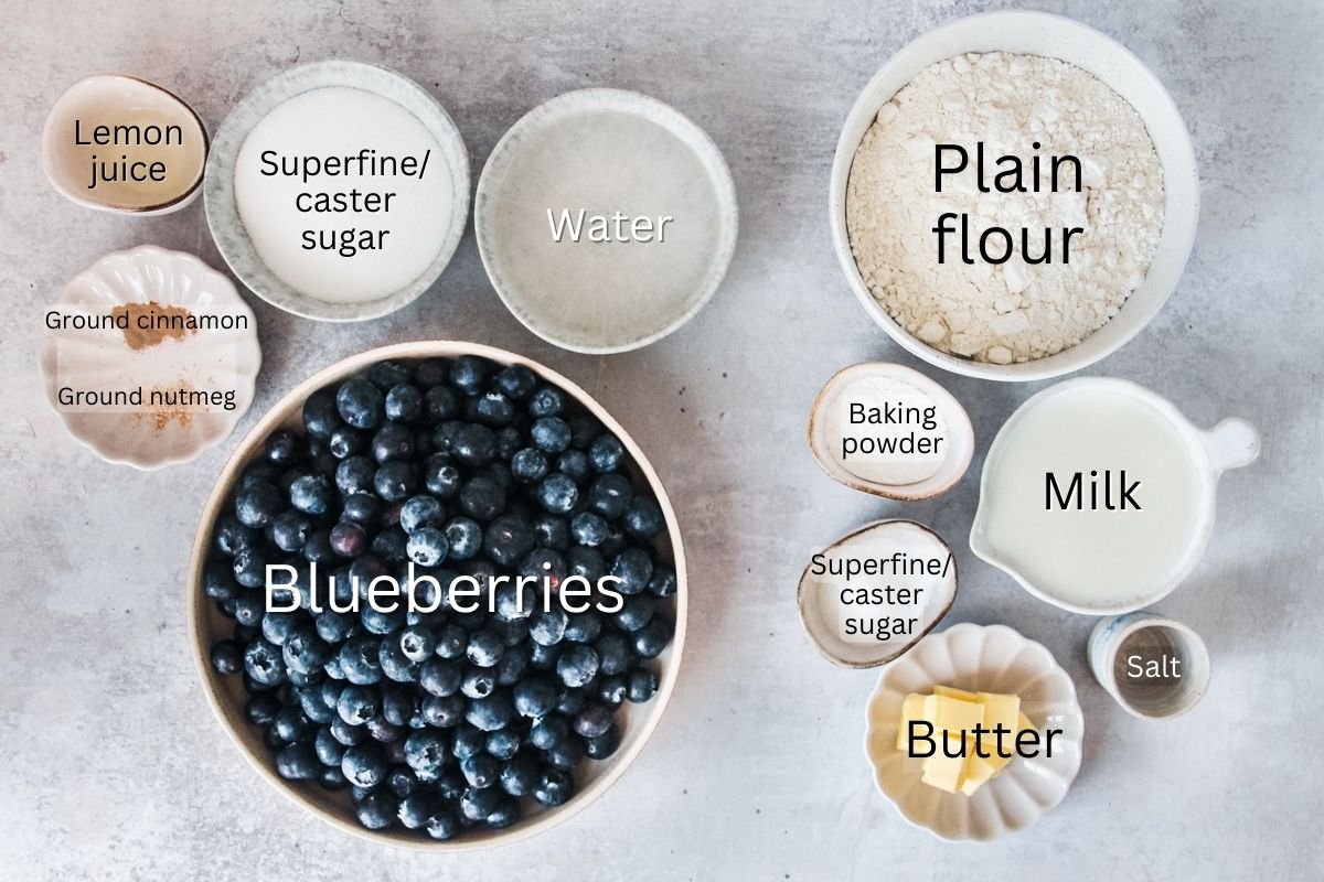Ingredients for Blueberry Cobbler or Blueberry Grunt are laid out on a light grey background in a variety of bowls.