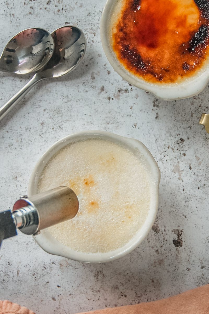 Sugar is caramelized with a blowtorch on top of a Earl Gray Creme Brulee in an individual ramekin on a light gray surface.