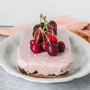 A no bake and no gelatin Cherry Cheesecake sits on a plate with fresh cherries on top on a light gray background.