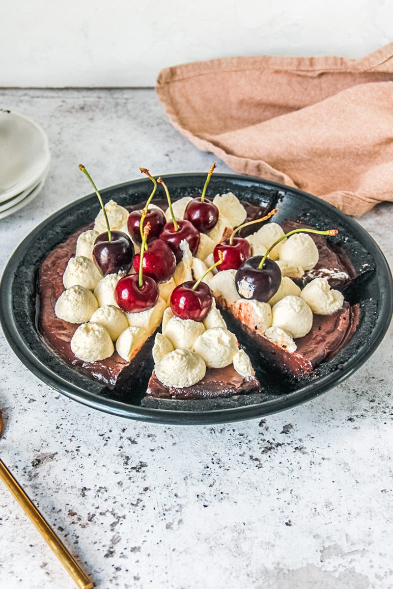 Slices are cut into a no bake chocolate cherry pudding pie in a black metal baking tin on a light gray surface.