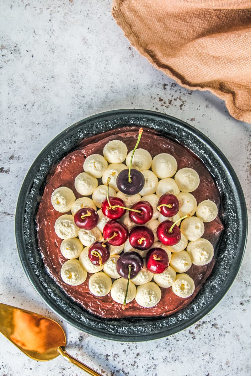 A no bake chocolate cherry pudding pie sits in a metal pie dish on a light gray surface.