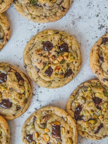 Pistachio chocolate chunk cookies lay on a light gray surface.