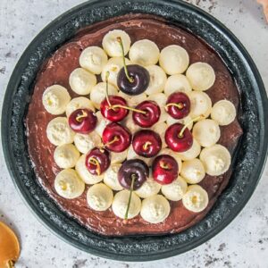 A no bake chocolate pudding cherry pie sits in a black metal pie dish on a light gray surface.