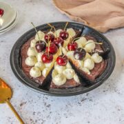 Slices are cut into a no bake chocolate cherry pudding pie in a black metal baking tin on a light gray surface.