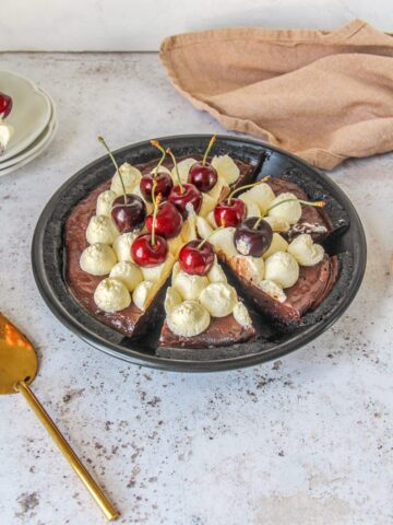 Slices are cut into a no bake chocolate cherry pudding pie in a black metal baking tin on a light gray surface.