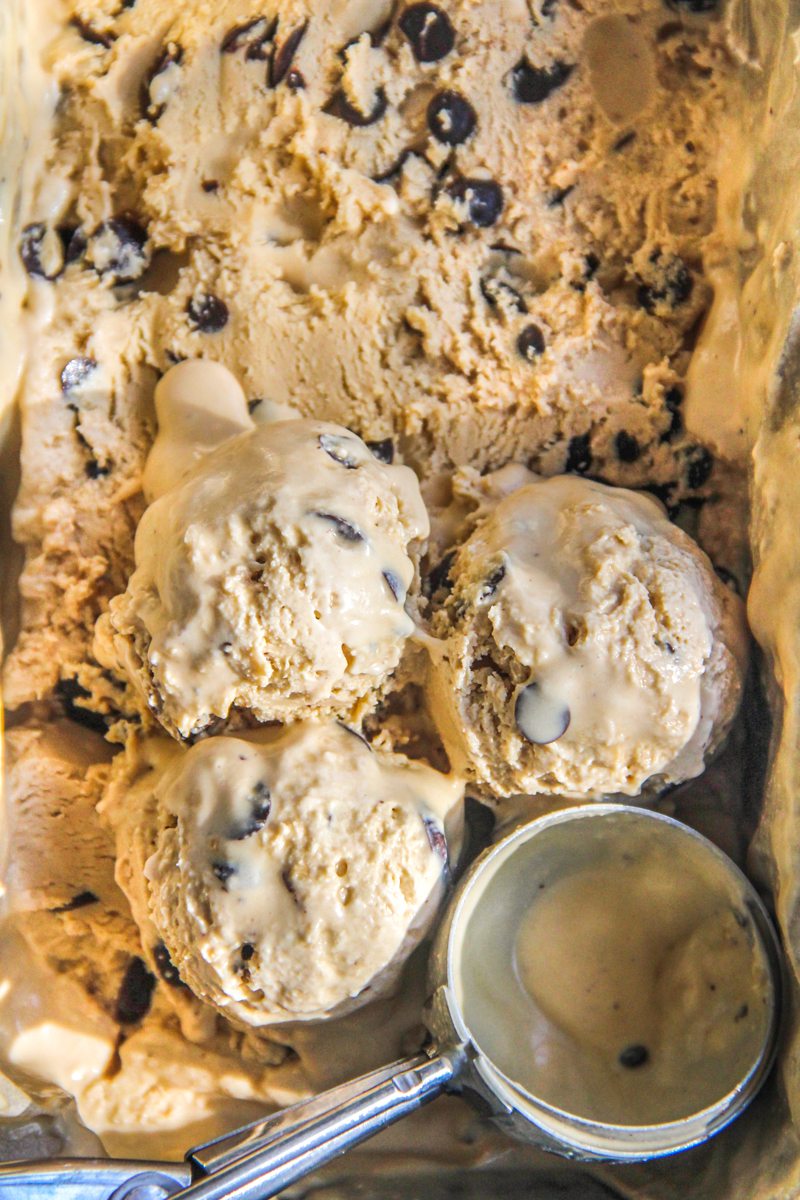 Coffee chocolate chip frozen custard sits with three scoops resting on top of the ice cream and an ice cream resting beside in the tin.