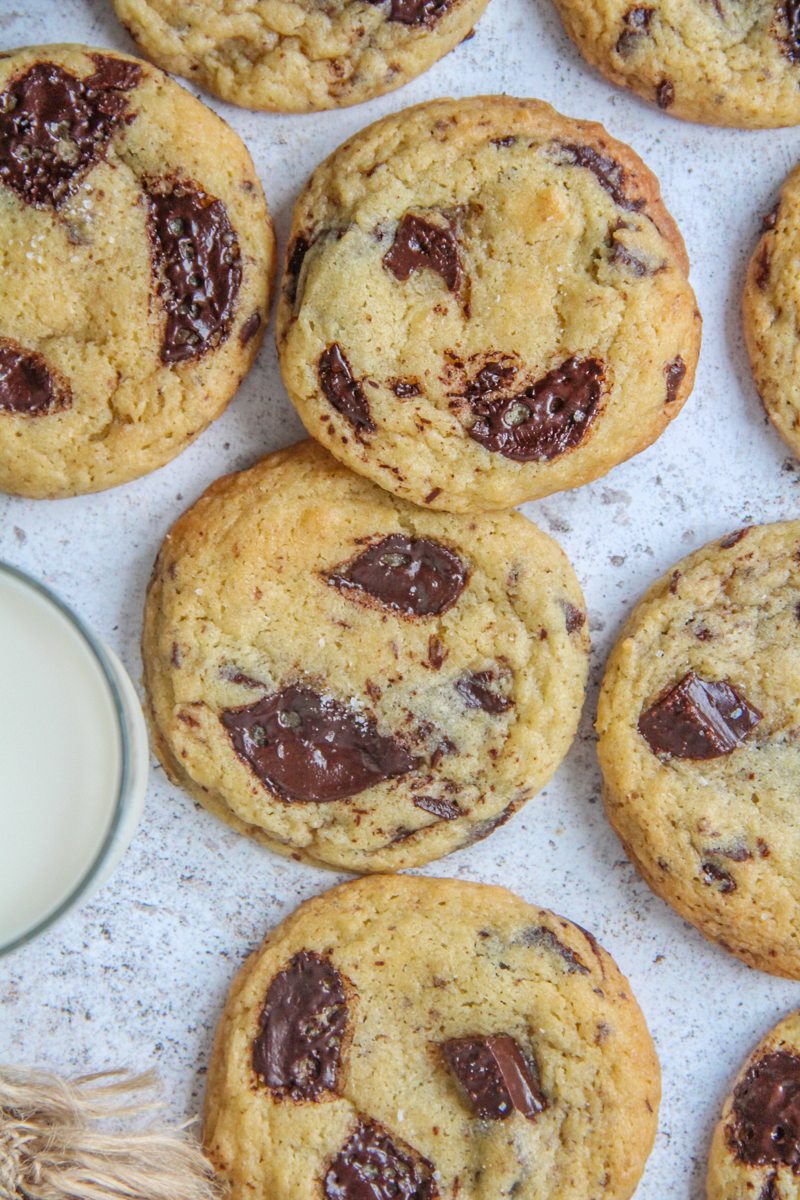 Chocolate chunk cookies lay on a light gray surface with a glass of milk beside.