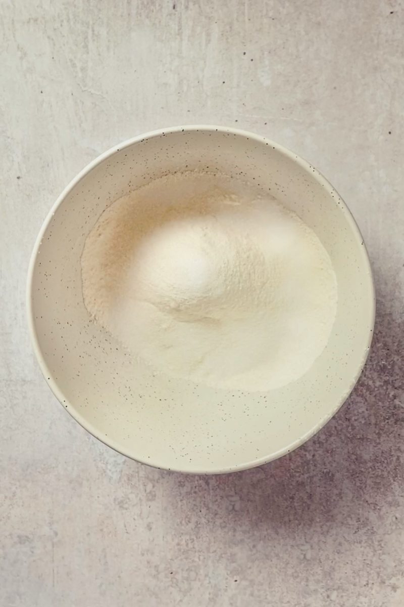 Dry ingredients for choux pastry sit in a white ceramic bowl on a gray surface.