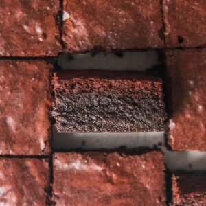 A fudgy brownie sits on its side above other slices of brownie.