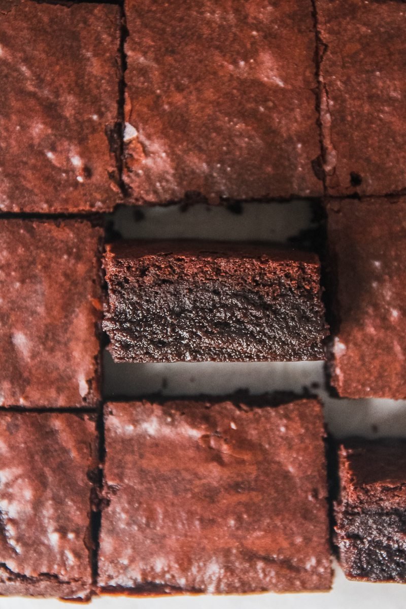 A fudgy brownie sits on its side above other slices of brownie.