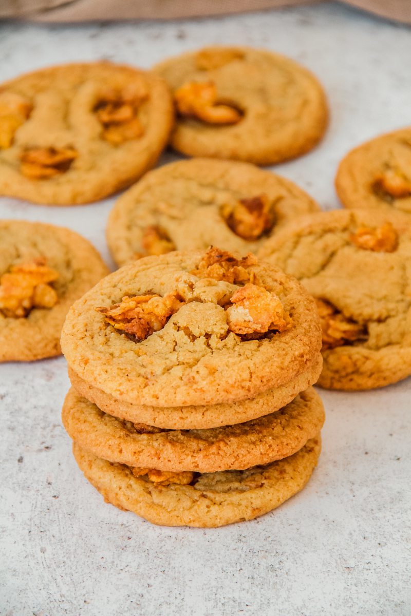 A stack of cornflake cookies sit on a light gray surface.
