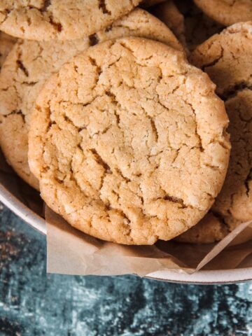 A close up of Cornish Fairing or British Ginger biscuits sitting on a rimmed ceramic plate lined with parchment paper above a green and white surface.