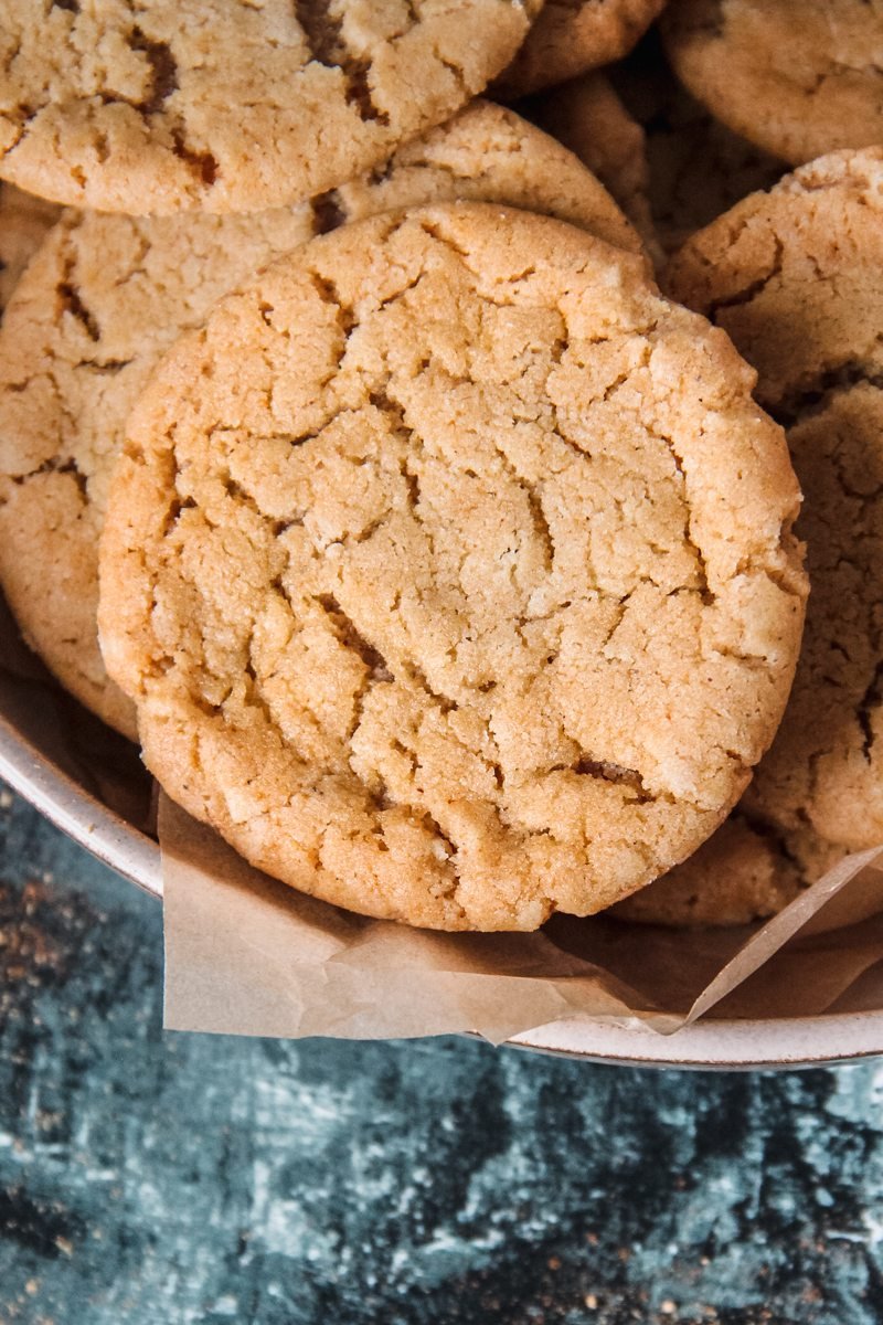 A close up of Cornish Fairing or British Ginger biscuits sitting on a rimmed ceramic plate lined with parchment paper above a green and white surface.