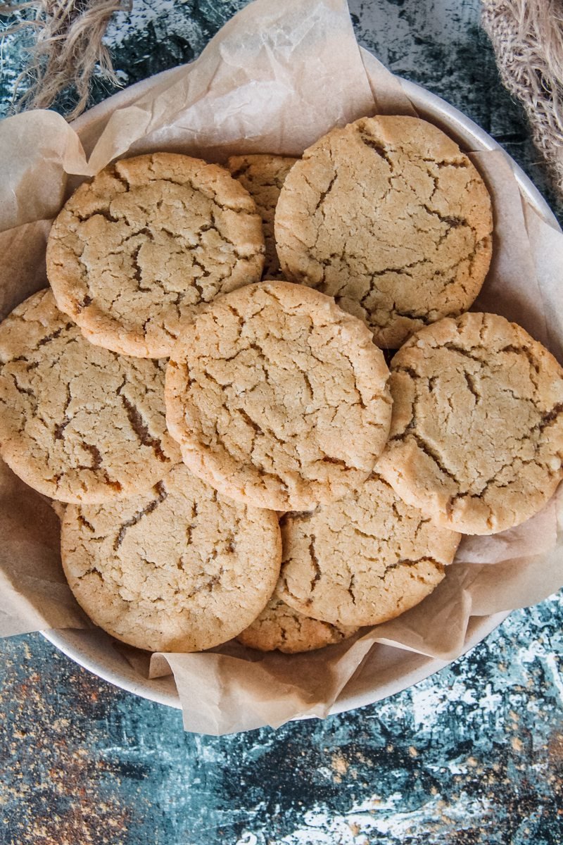 British Ginger Biscuits also known as Cornish Fairing sit on a rimmed ceramic plate lined with parchment paper above a green and white surface.