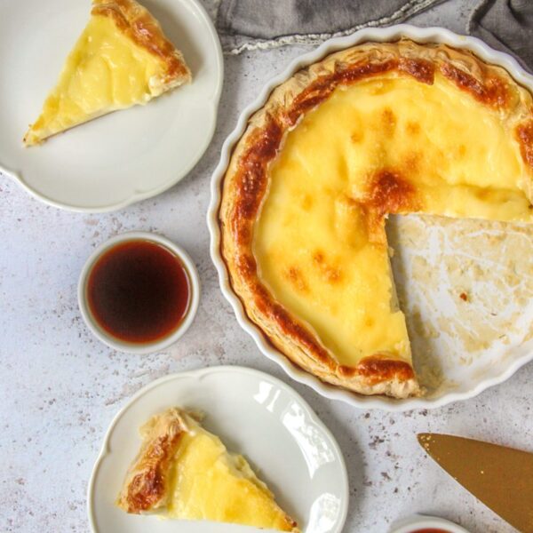 Belgian Cream Pie - Tarte a la creme sits on a light gray surface with a portion remaining in the ceramic baking dish and slices on fluted white ceramic plates.