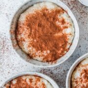 Creamy Greek rice pudding sits served in individual bowls in pale blue ceramic bowl on a light gray surface.