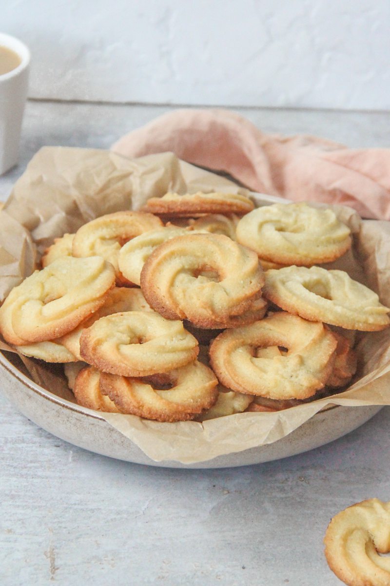 Danish butter cookies sit in a deep ceramic plate lined with parchment paper on a gray surface.