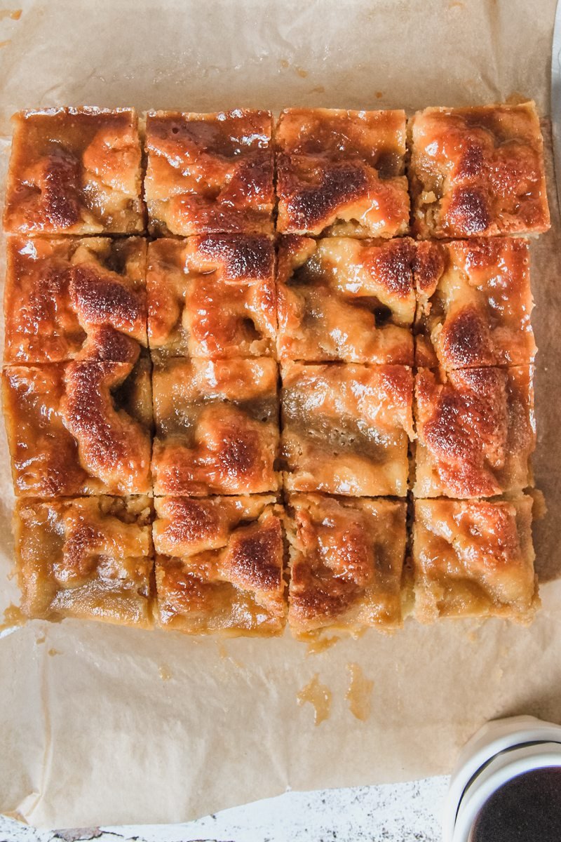 A slice of Brunsviger sits on a brown parchment paper surface with it's caramelized topping and uneven cake texture visible.