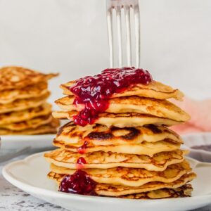 A fork is pierced into a stack of rice pudding pancakes on a white ceramic plate on a gray surface.