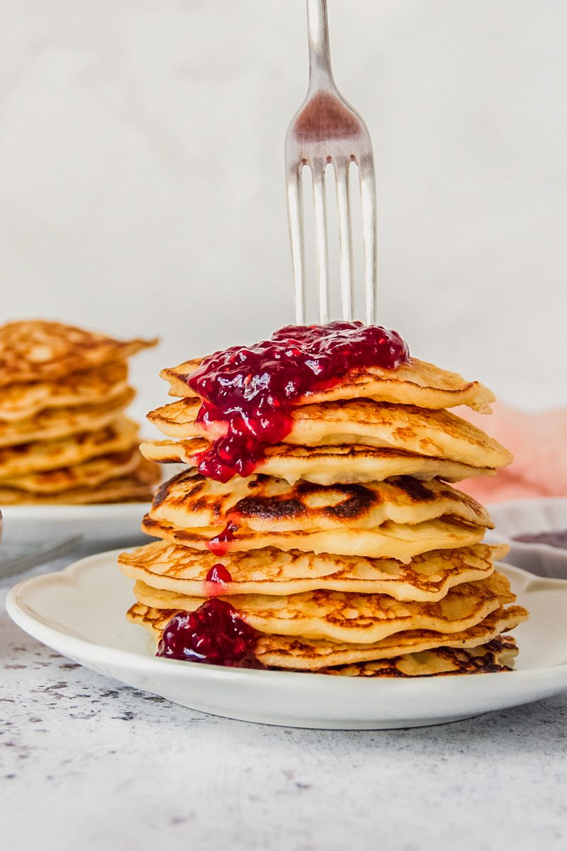 A fork is pierced into a stack of rice pudding pancakes on a white ceramic plate on a gray surface.