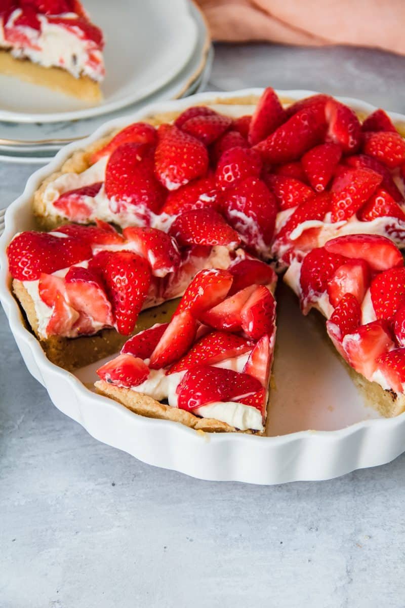 Slices of Danish strawberry tart sit in the ceramic tart dish on a light grey background.
