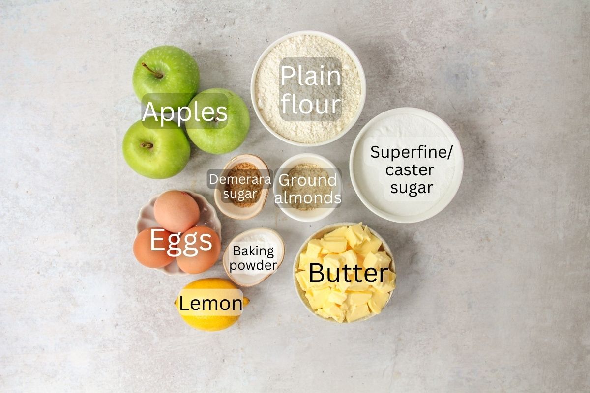 Ingredients for Dorset Apple Cake sit in a series of bowls on a gray surface.