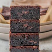 A stack of double chocolate brownies sit on each other on a light gray surface.