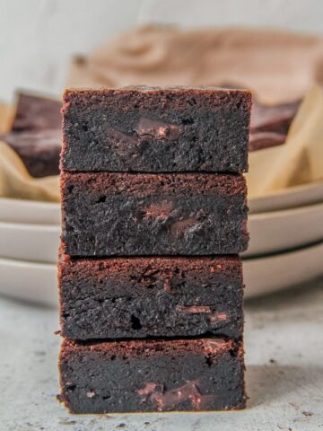 A stack of double chocolate brownies sit on each other on a light gray surface.