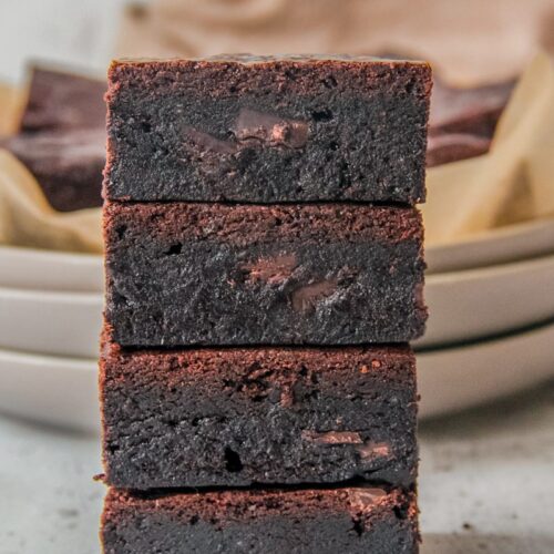 A stack of double chocolate brownies sit on each other on a light gray surface.
