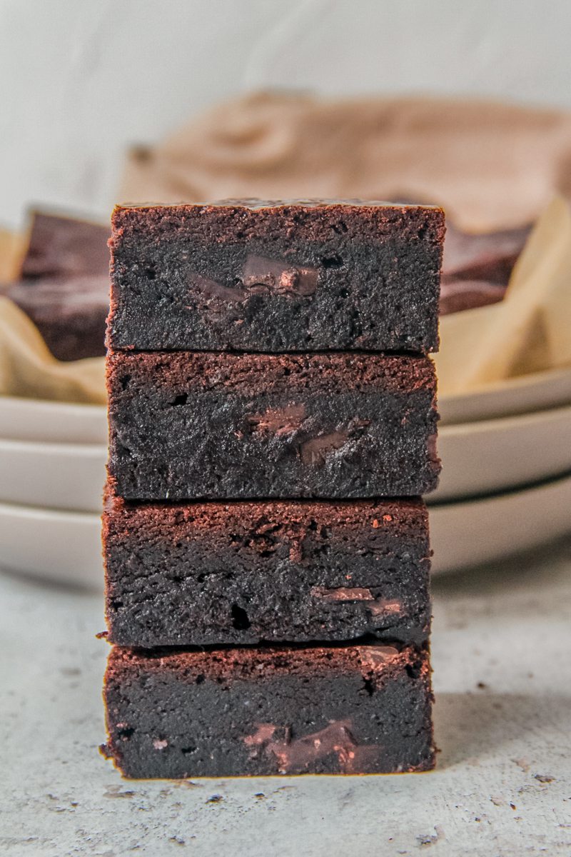 A stack of double chocolate brownies sit on each other on a light gray surface.