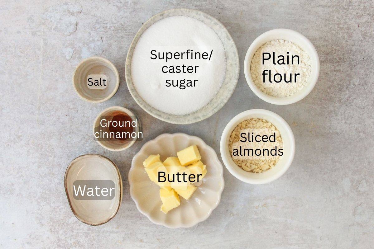 Ingredients for Dutch Kletskoppen - Almond Lace Biscuits sit in a series of bowls on a gray surface.