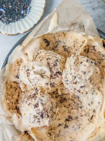 Scoops of earl grey semifreddo with Stracciatella ice cream sit a lined tin round tin with a small plate of loose earl gray tea beside on a gray surface.