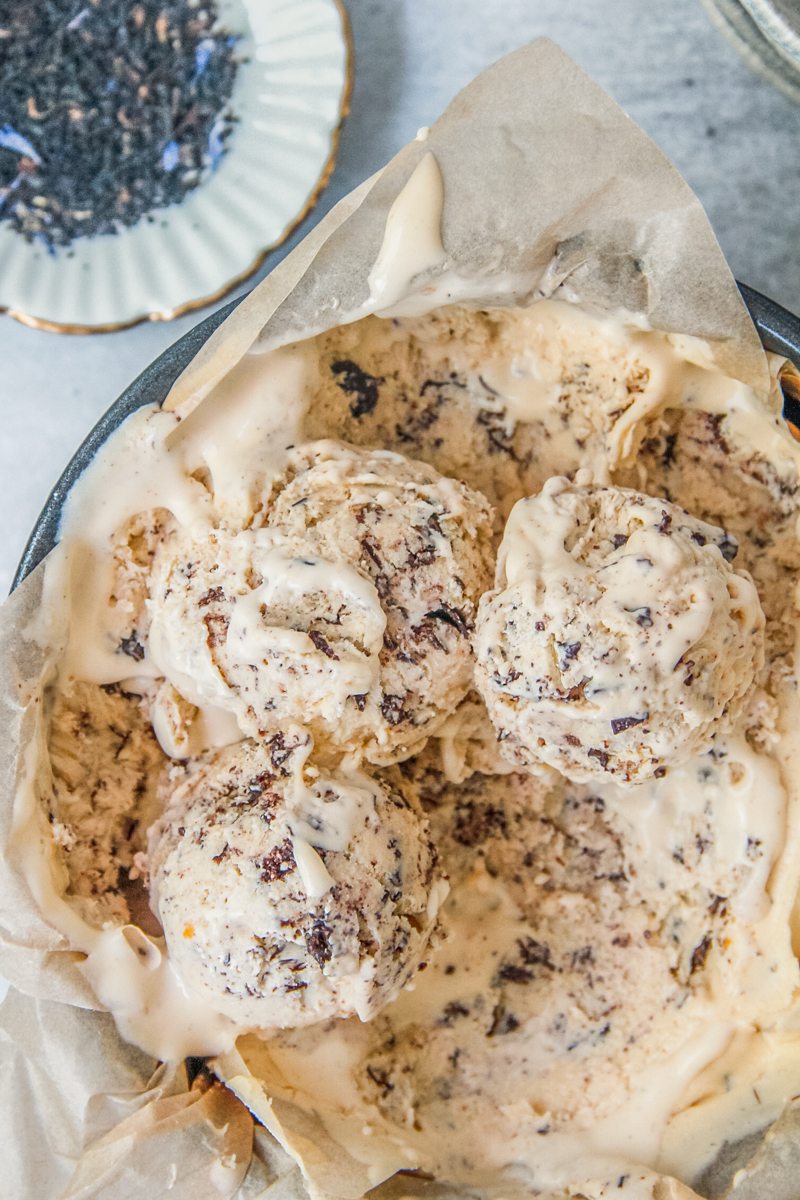 Scoops of earl grey semifreddo with Stracciatella ice cream sit a lined tin round tin with a small plate of loose earl gray tea beside on a gray surface.