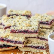 Estonian Jam Bars (Klassikaline Purukook) sit stacked on each other on a wooden board on a pink surface.